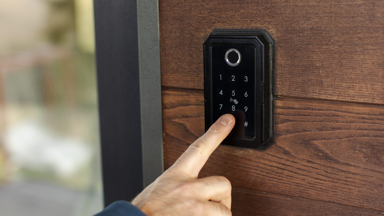 A hand pressing the keypad of a keyless entry lock beside a wooden entry wall