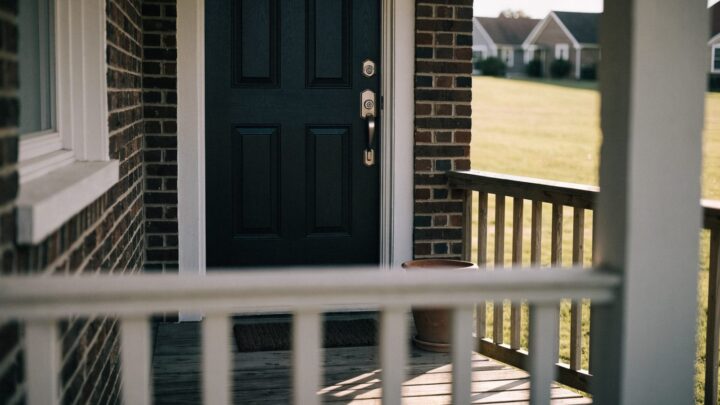 A navy front door with a satin nickel deadbolt above the handleset, seen from the porch in morning light.