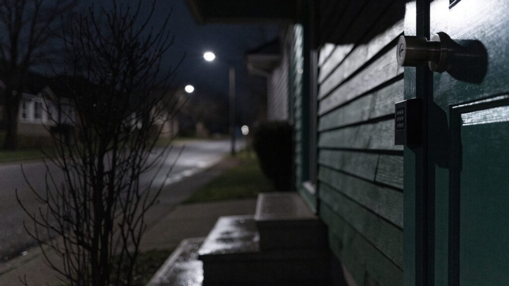 A dark front porch at night with a distant street lamp catching the metal edge of a deadbolt