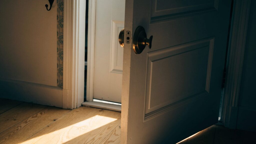 A front door ajar with the deadbolt still thrown, morning light falling across an empty entryway