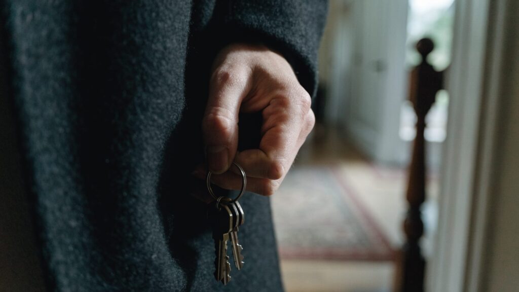 A hand pulling a small ring of house keys from a coat pocket at an open front door