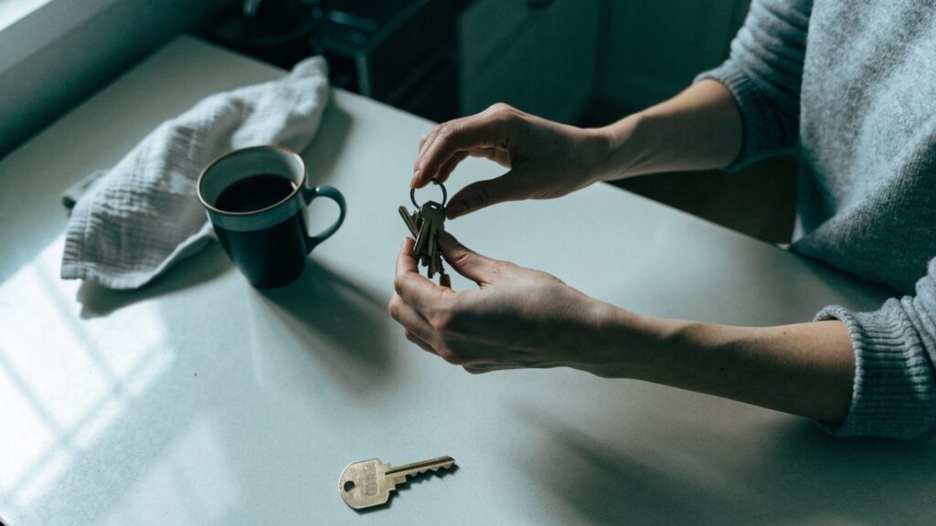 Hands sorting a ring of apartment keys on a kitchen counter beside a second key set and a coffee mug