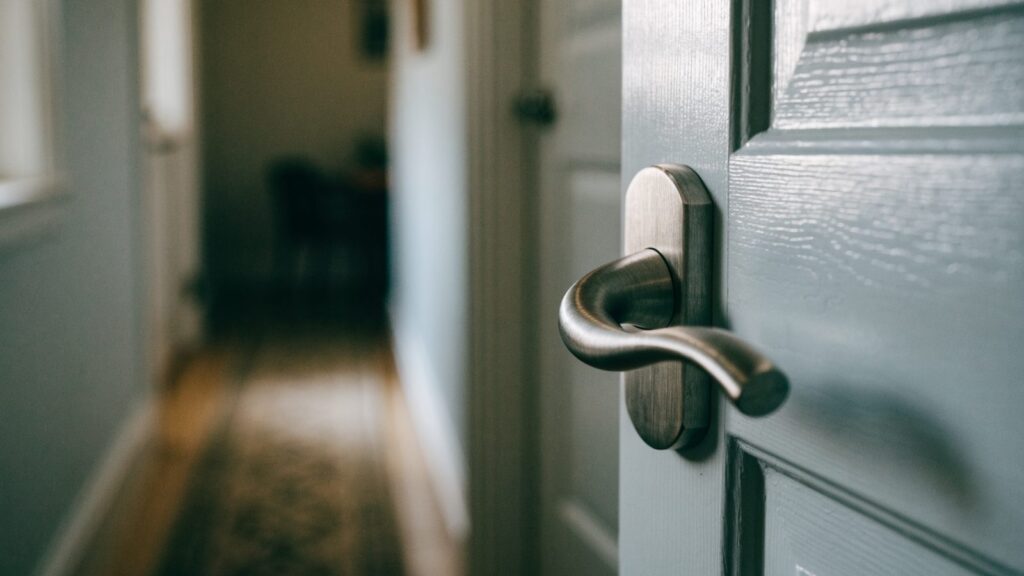 Brushed nickel lever handle on a pale painted interior door with the hallway blurred behind it