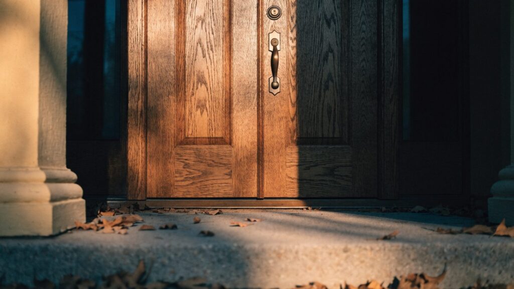 Tall stained wood front door with a full-length handleset, thumb piece below a separate deadbolt
