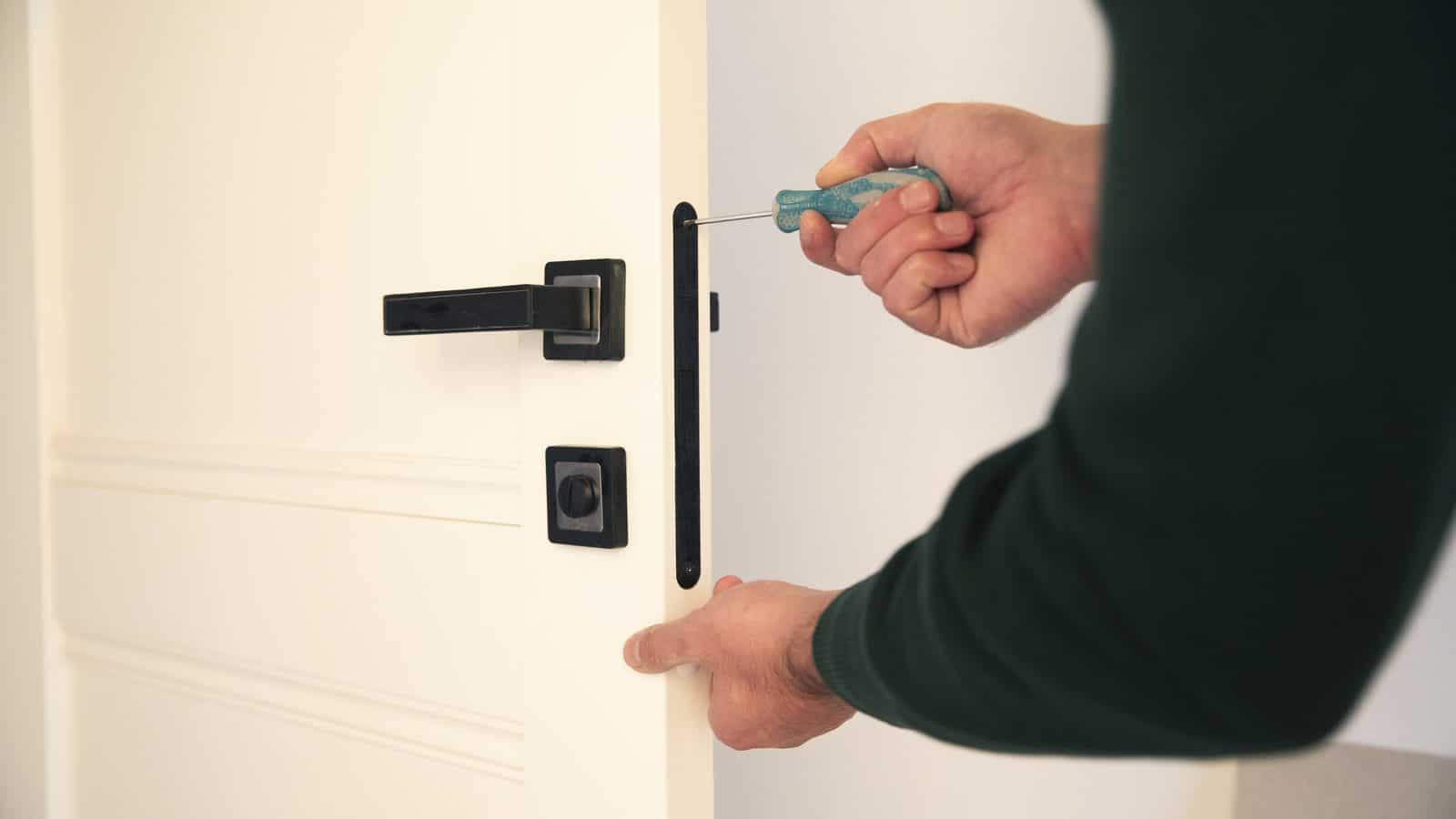 A hand holding a key beside a black lever handle and separate deadbolt on a white door