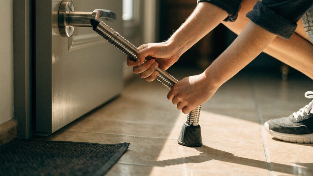 Hands adjusting a steel security bar braced from a tile floor to the lever handle of an apartment door