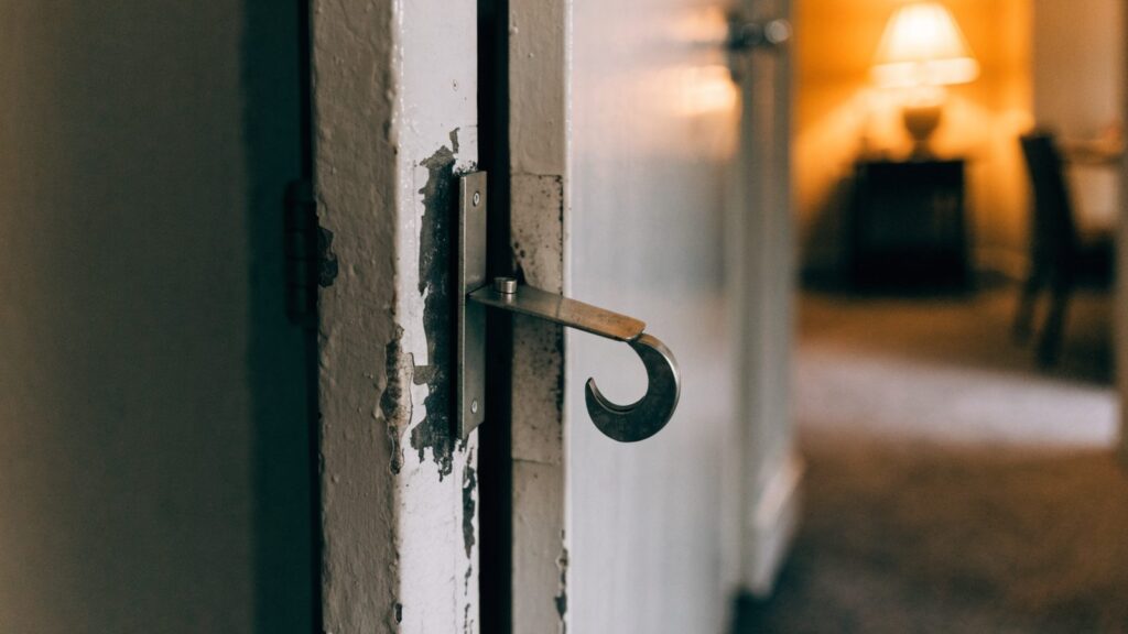 Flat steel portable door lock hooked into the strike opening of an apartment door left slightly ajar