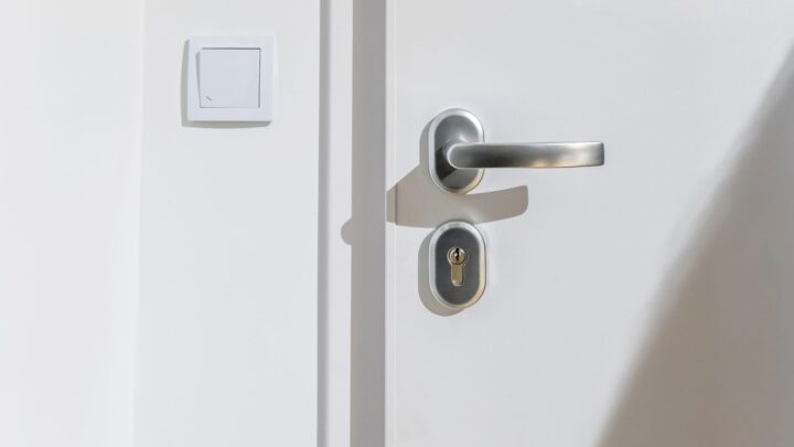 A white apartment entrance door with a lever handle and cylinder lock in daylight
