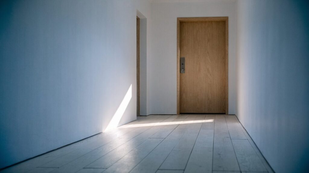 Minimalist entry hall with a slim lock body on a light oak door and morning sun across pale floorboards