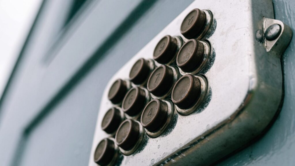 Worn rubber buttons and scratched trim on a weathered keypad deadbolt, seen close up at a steep angle
