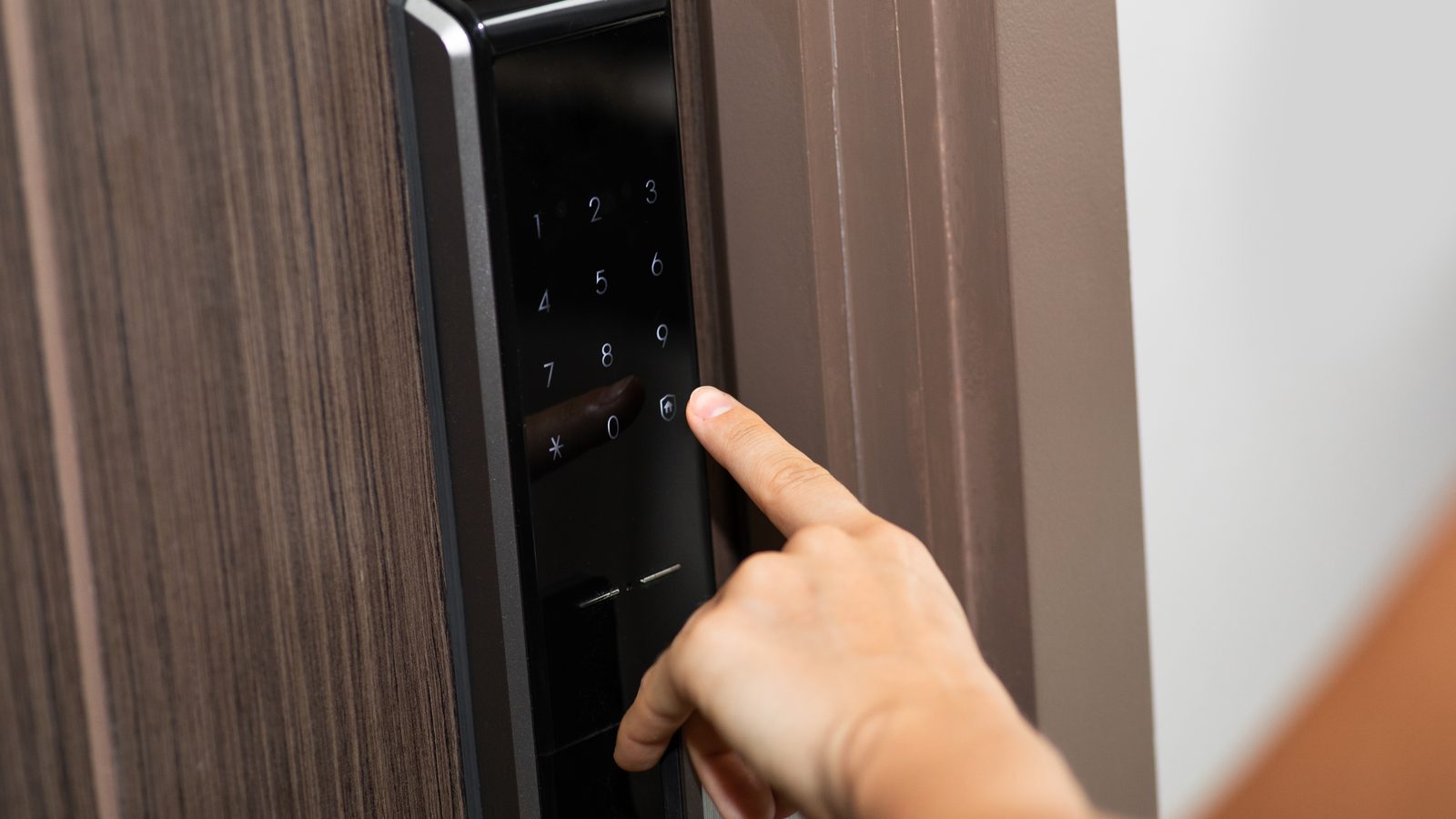 A finger pressing a digit on an illuminated smart lock keypad in an apartment doorway