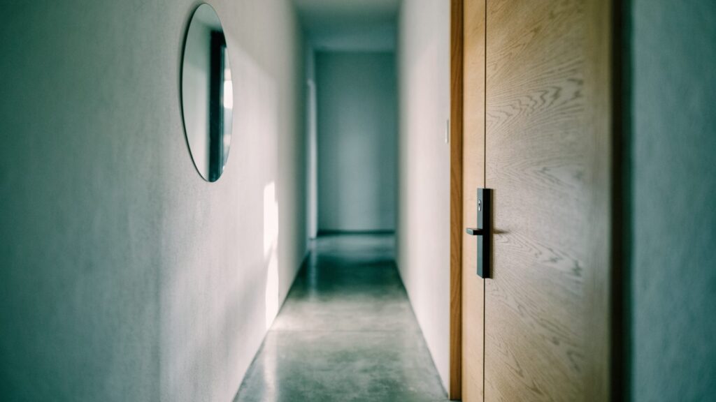 Slim lock body on a pale flush front door seen from inside an entry hall, mirror reflecting daylight