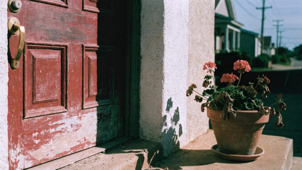 A sun-bleached deadbolt and handle on a faded red south-facing door in hard midday light