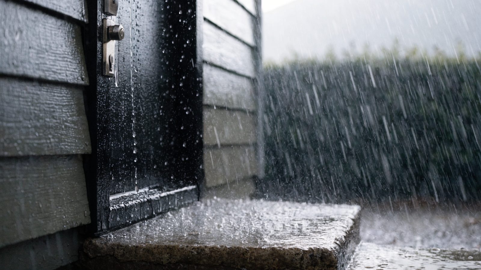 Rain streaming down an unsheltered exterior door and its lock during a downpour