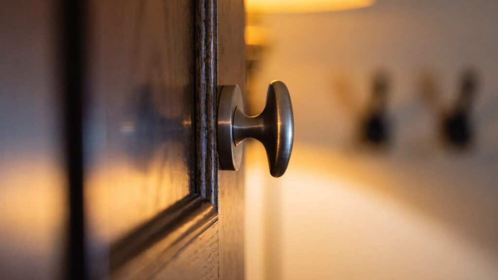 Side view of an oval thumbturn on a dark stained apartment door showing how far it stands off the rose