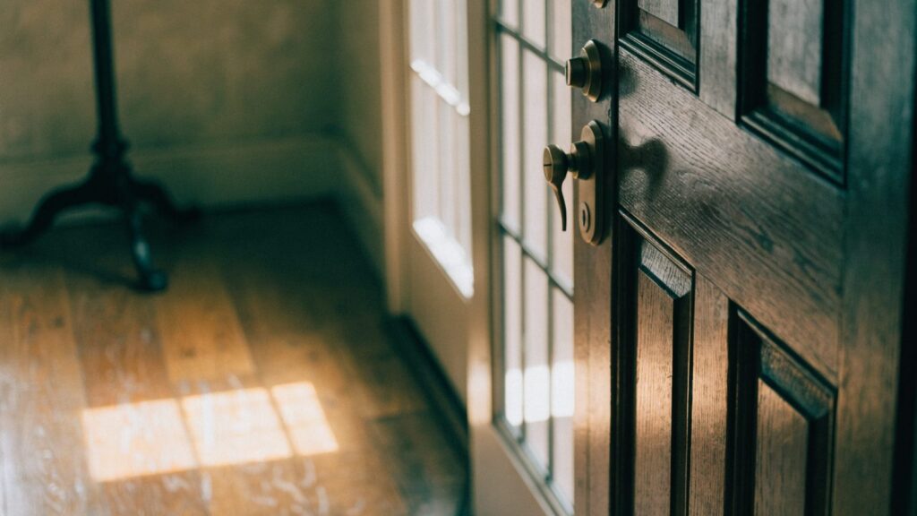 Front door with a tall glazed sidelight panel beside the deadbolt, daylight falling across the entry floor