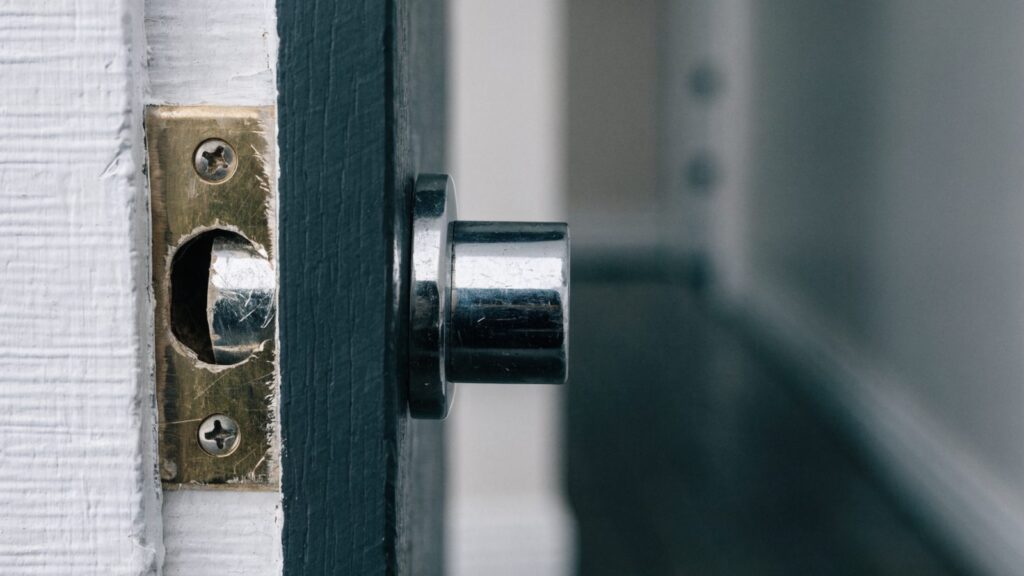 Deadbolt jammed against the lip of a misaligned strike plate on a white painted door jamb