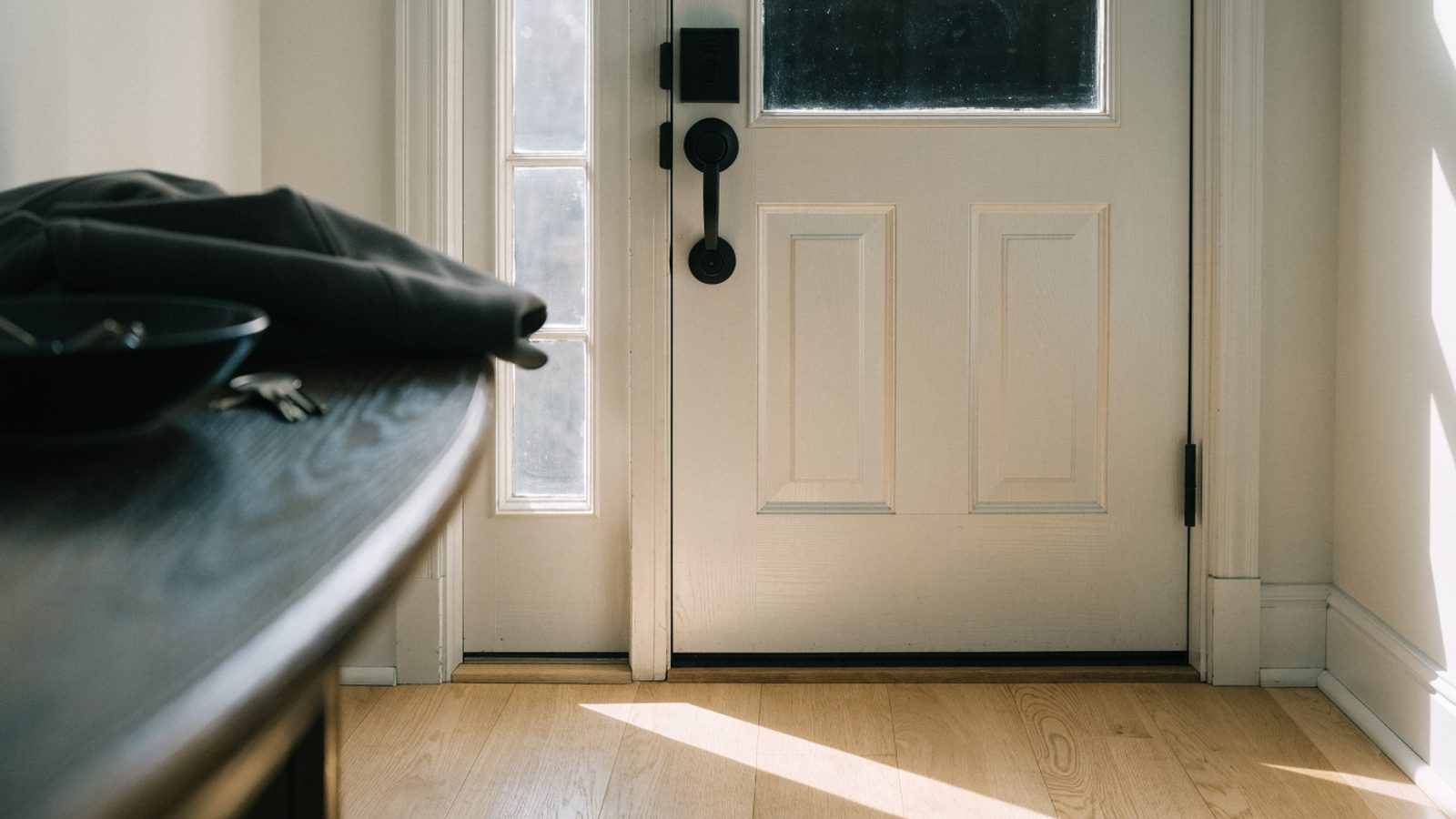 Motorized smart deadbolt in the unlocked position on the inside of a white front door in morning light
