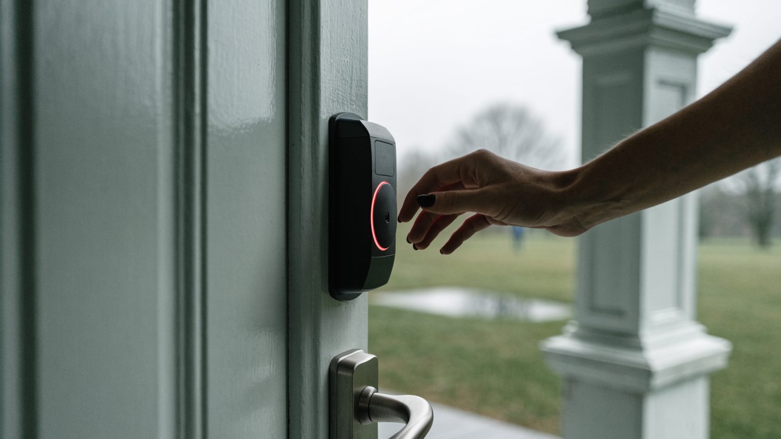 A hand leaving a smart lock keypad as a red indicator ring glows on an exterior front door