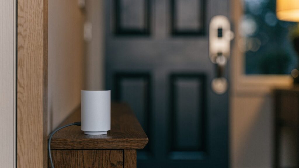 A small smart home hub on a hallway table with a smart lock on the front door behind
