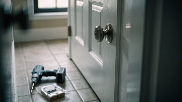A white interior door with a single keyed knob and no deadbolt above it, drill and boxed lock waiting on the floor