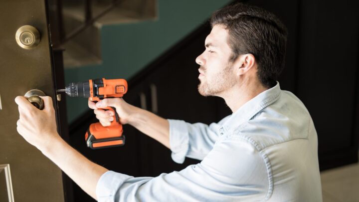 A tradesman using a cordless drill to fit door hardware in a hallway