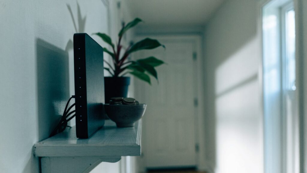 A home router on a hallway shelf with its indicator lights on and the front door blurred far down the corridor.