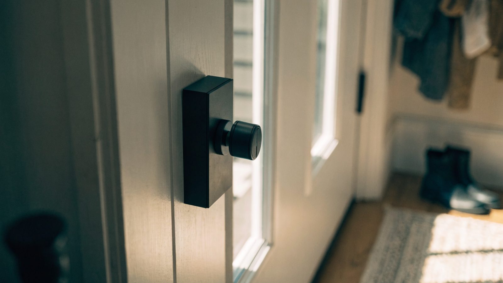 A black keypad smart deadbolt on a white front door, seen from inside a sunlit entryway