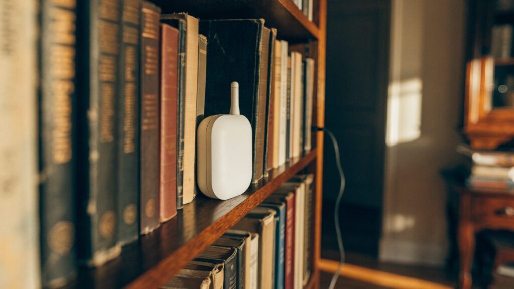 A small home automation hub with a short antenna on a bookshelf, a thin ethernet cable dropping behind it.