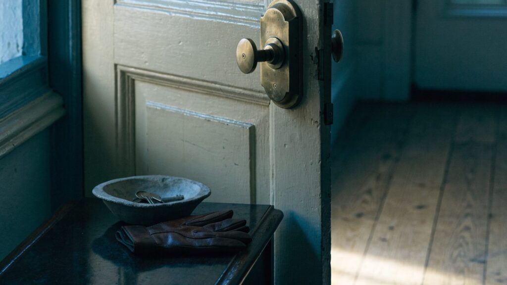 Interior face of a painted front door with the deadbolt thrown, keys in a shallow bowl on a console table below.