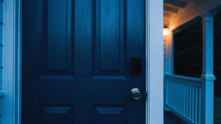 Keypad smart deadbolt on a navy front porch door at dusk