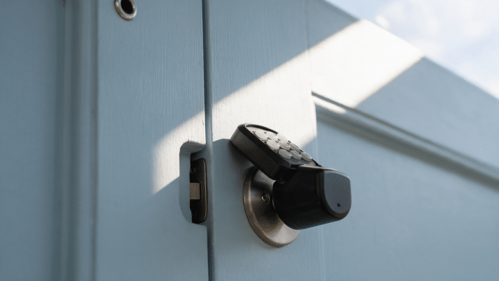 Keypad smart deadbolt on a pale blue front door in midday sun.