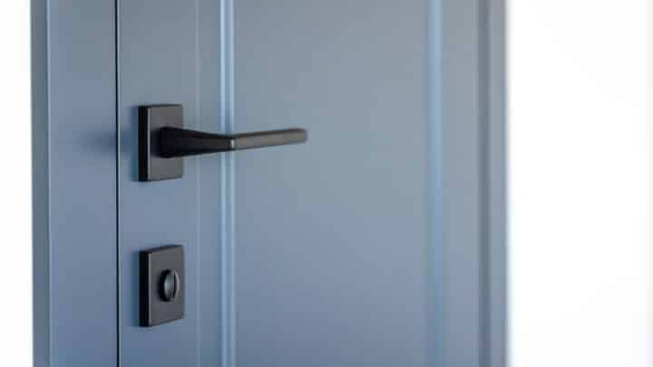 A slate-blue flush interior door with a matte black lever handle and a round privacy turn-lock below it.