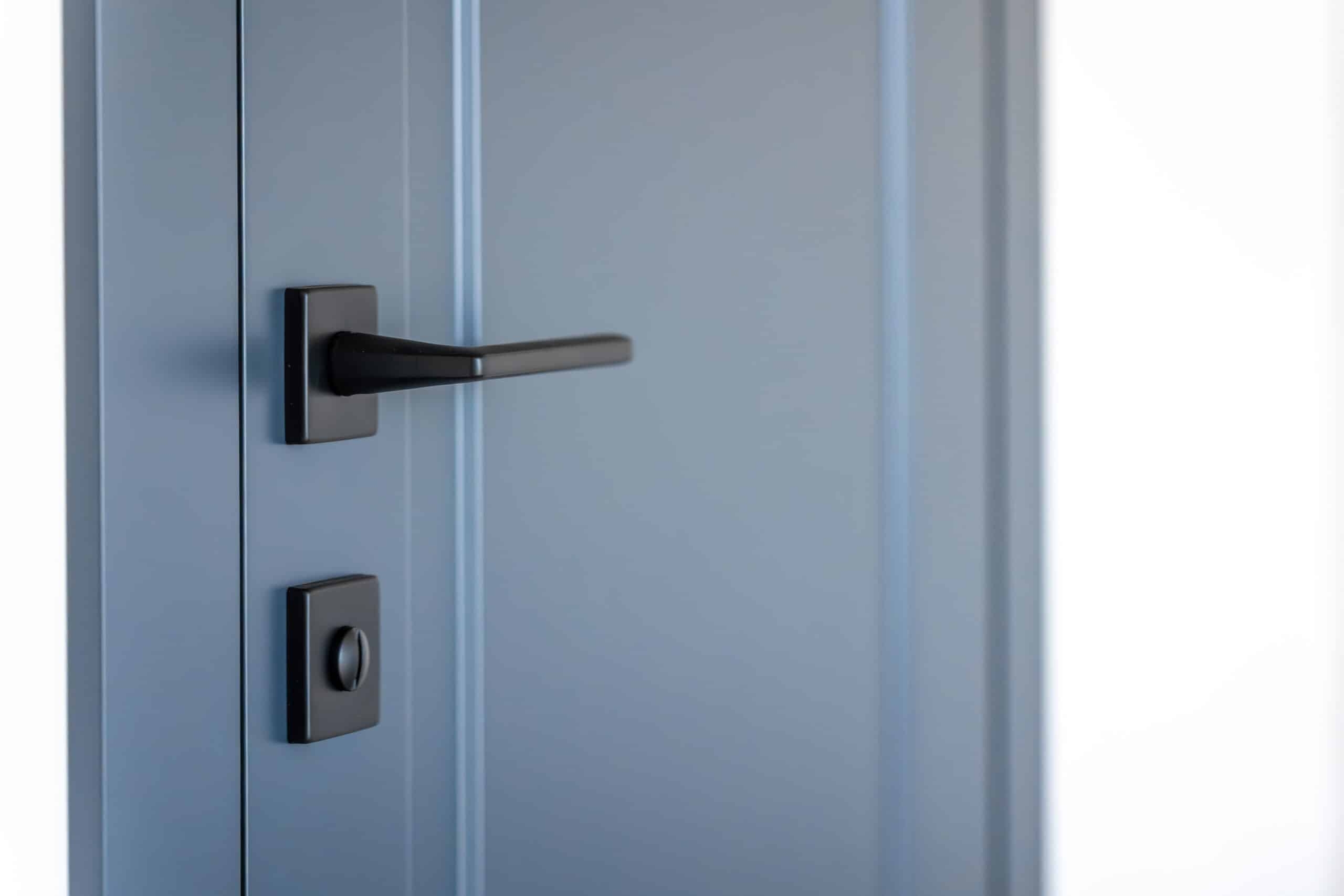 A slate-blue flush interior door with a matte black lever handle and a round privacy turn-lock below it.