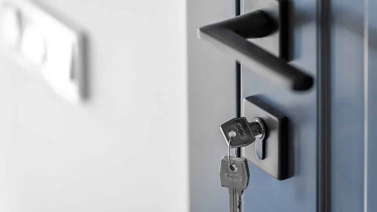 A set of keys hanging from a black deadbolt lock on a dark blue front door