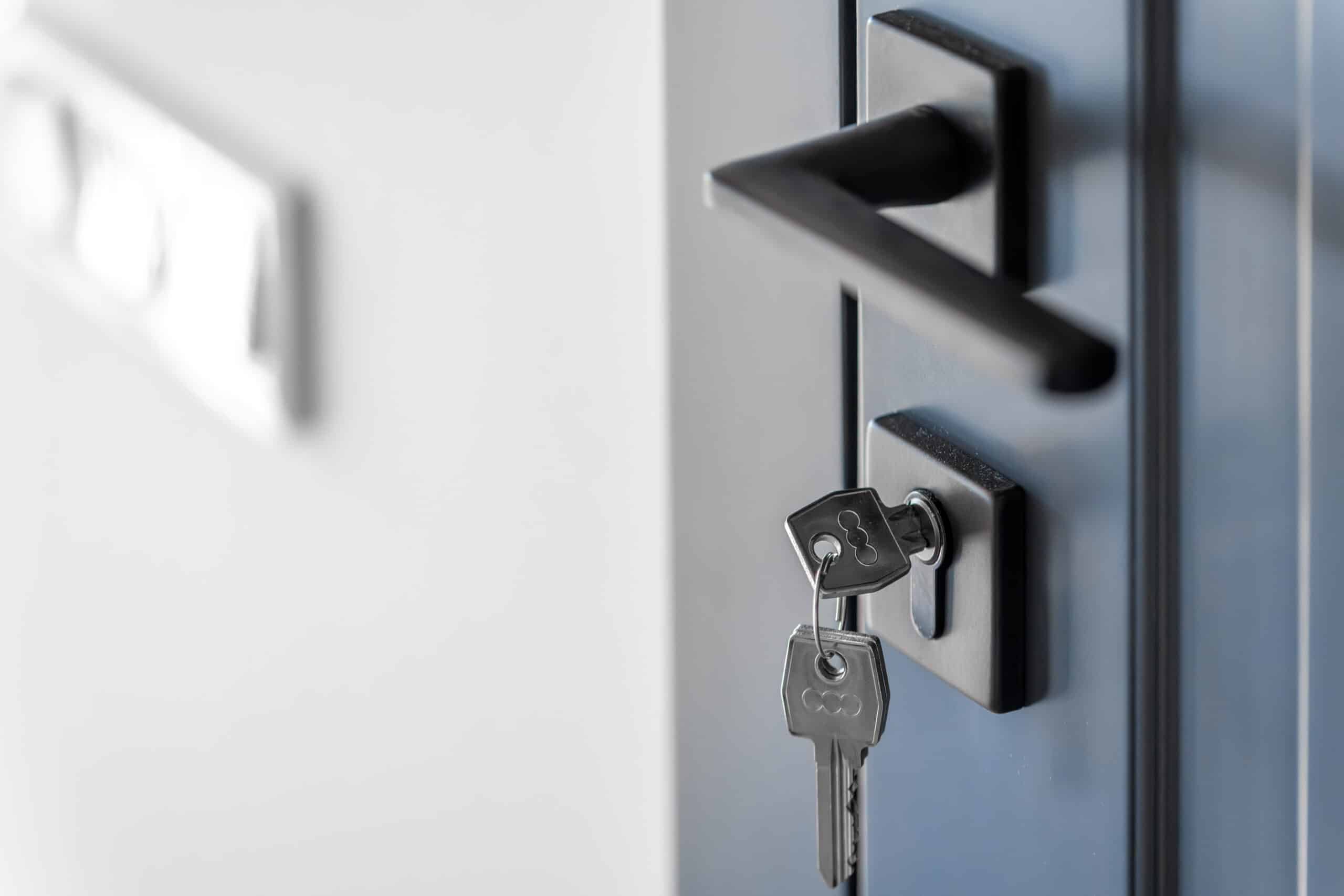 A set of keys hanging from a black deadbolt lock on a dark blue front door